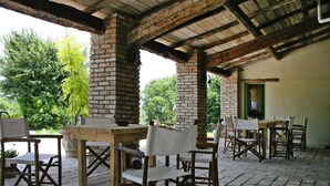 An outdoor patio area with rustic wooden tables and chairs, brick pillars, and a view of greenery.