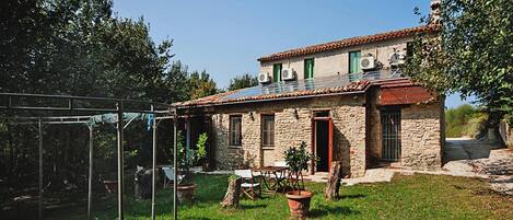 A stone house with a tiled roof, a small garden, and a metal fence.