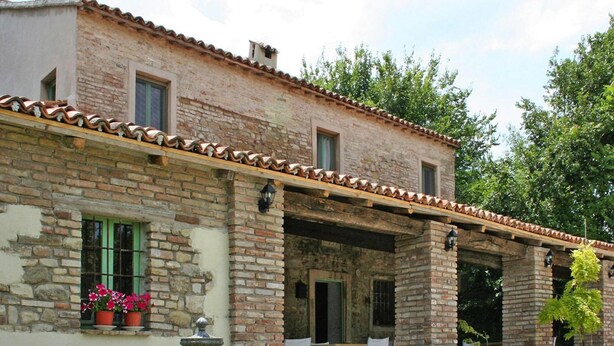 A rustic stone building with a tiled roof, outdoor seating, and potted plants.
