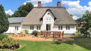A white house with a thatched roof, a wooden deck, and a garden. - Reetgedecktes Ferienhaus in Humptrup (Humptrup)