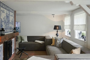 A living room with a fireplace, a sofa, a lamp, and a view of the outside through large windows. - Reetgedecktes Ferienhaus in Humptrup (Humptrup)