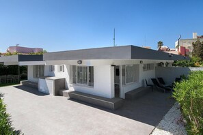 Une maison moderne avec un toit plat, de grandes fenêtres et un patio aménagé avec du mobilier d’extérieur.