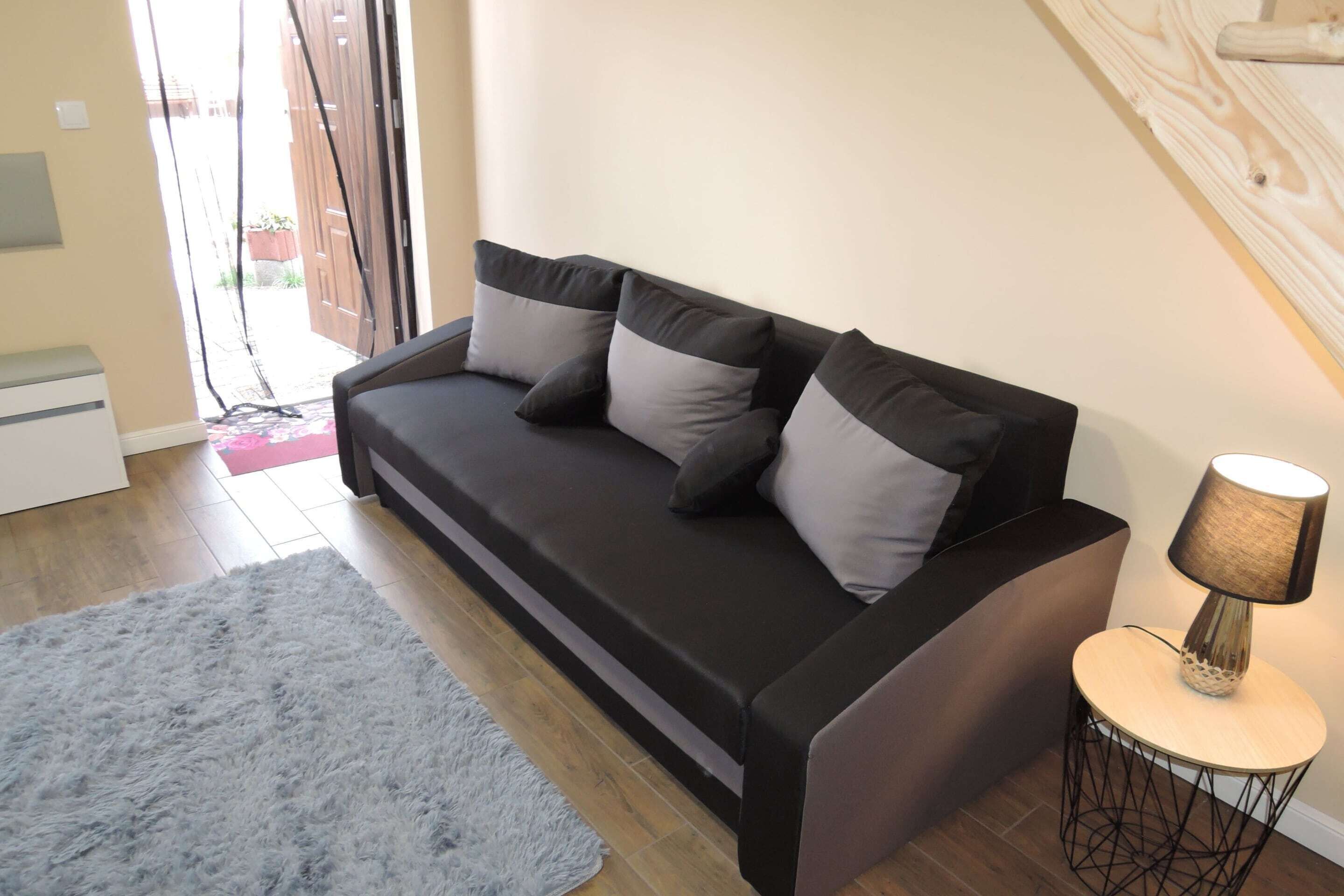 A modern living room with a dark sofa, a round side table with a lamp, and a fluffy rug.