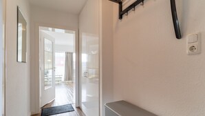 A hallway with a door leading to a balcony, a bench, and a wall-mounted light fixture. - Ferienwohnung, St. Peter-ording (St. Peter-Ording)