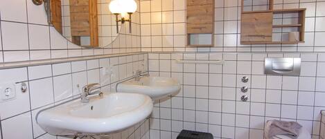 A bathroom with two sinks, a toilet, a trash bin, and wooden cabinets above the sinks.