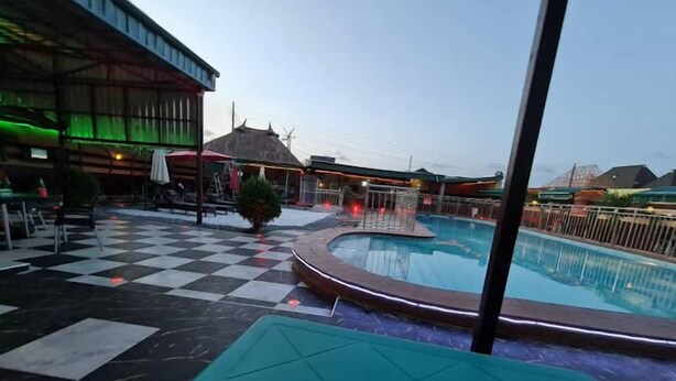 A pool area with a checkered floor, a lounge area, and a building with a green-lit exterior. - Rolak Hotel and Suites (Ijebu Ode)