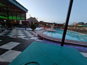 A pool area with a checkered floor, a lounge area, and a building with a green-lit exterior. - Rolak Hotel and Suites (Ijebu Ode)