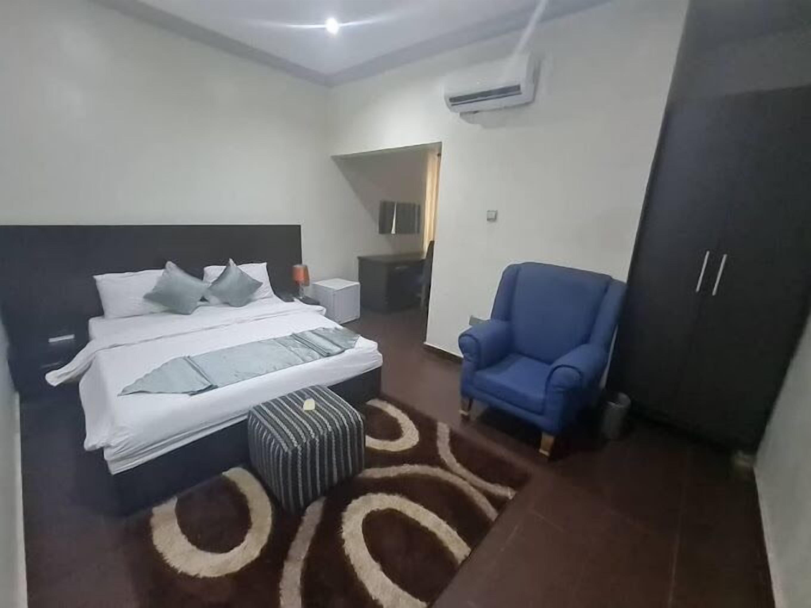 A bedroom with a bed, a blue armchair, a wardrobe, and a small ottoman.