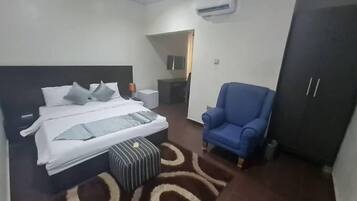 A bedroom with a bed, a blue armchair, a wardrobe, and a small ottoman.