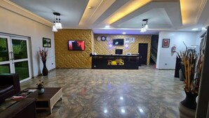 A reception area with a marble floor, a reception desk labeled 'ROTS', a television mounted on the wall, and a large window on the left. - Rolak Hotel and Suites (Ijebu Ode)