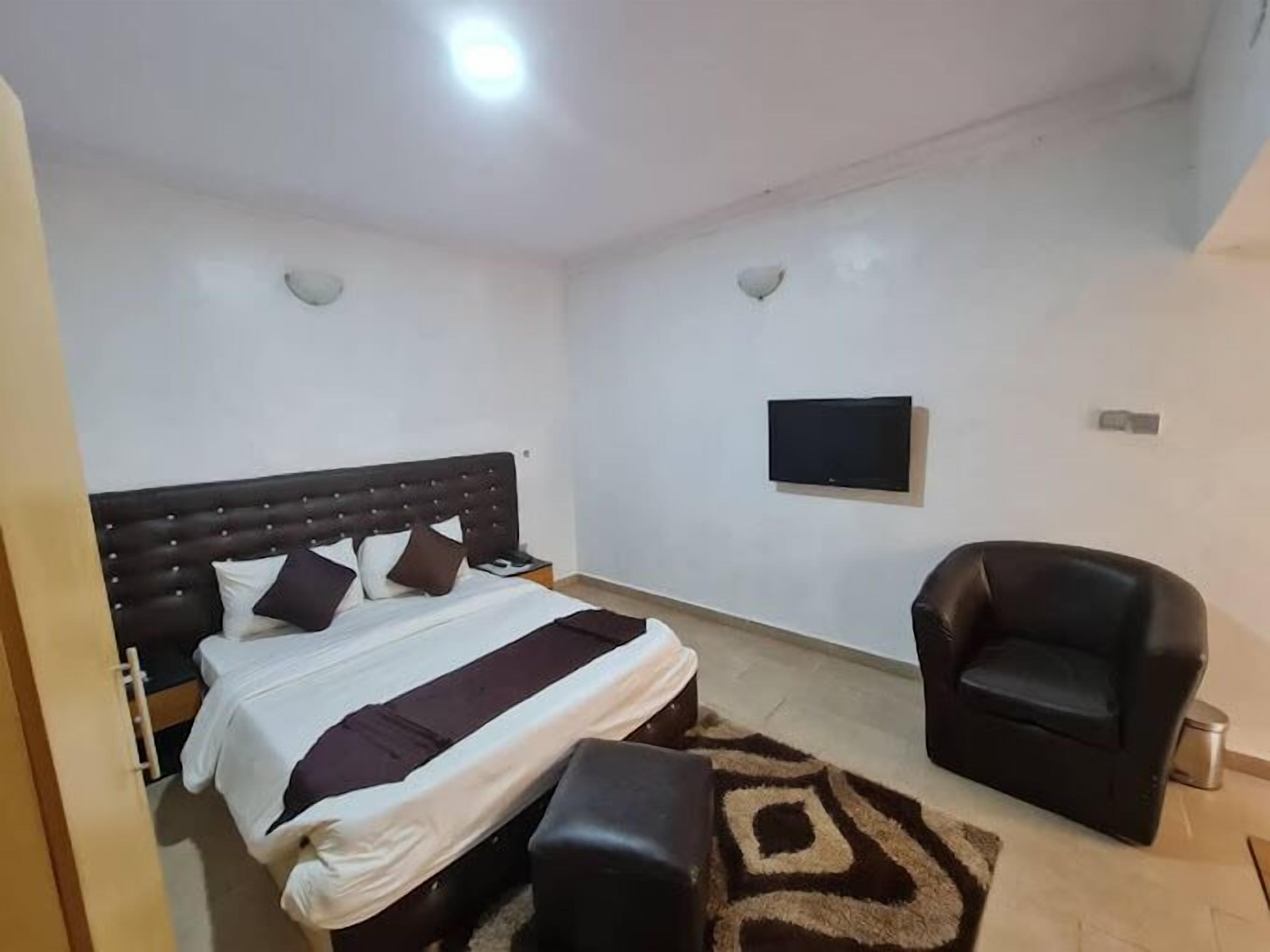A bedroom with a bed, a TV mounted on the wall, a chair, and a patterned rug.