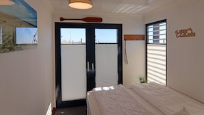 A bedroom with a bed, a large window, a door with a view, and a ceiling light fixture.