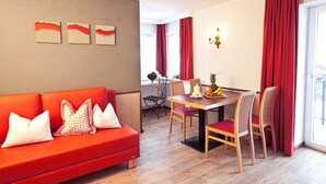 A modern living room with a red sofa, a dining table with chairs, and a view of the outdoors through large windows.