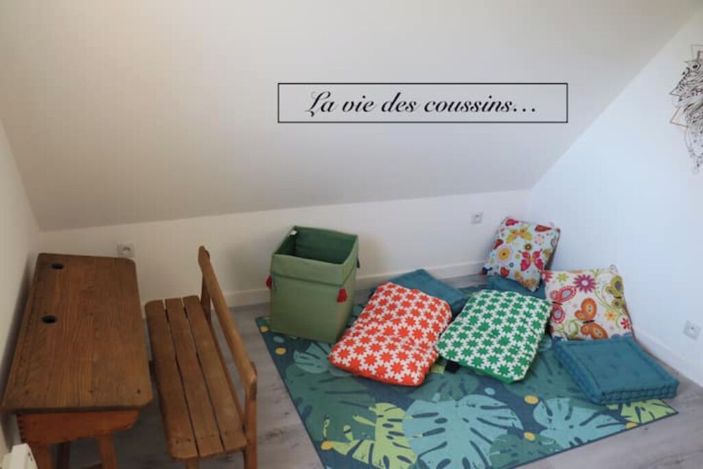 Ein kleines Zimmer mit Holztisch und Bank, bunten Kissen und einer Wand mit dekorativem Muster.
