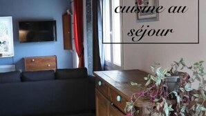 A cozy living room with a wooden ceiling, a sofa, a TV, and a wooden cabinet with plants. - Un Séjour Nature au Coeur de L'histoire (Nonant)
