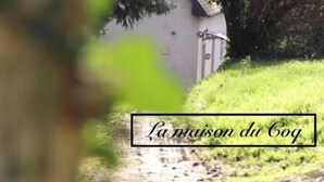 A rustic stone structure with a small white building in the background, surrounded by greenery. - Un Séjour Nature au Coeur de L'histoire (Nonant)
