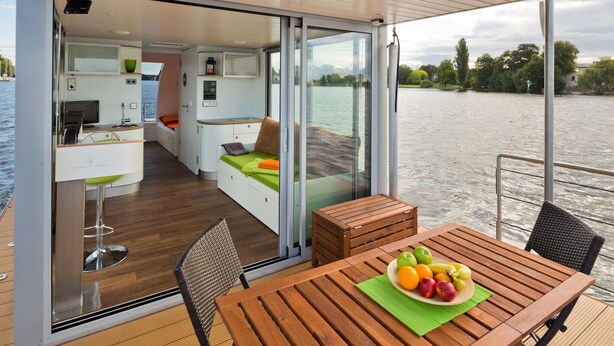 Un intérieur de bateau moderne comprenant un coin repas, une cuisine et un espace détente au bord de l’eau.