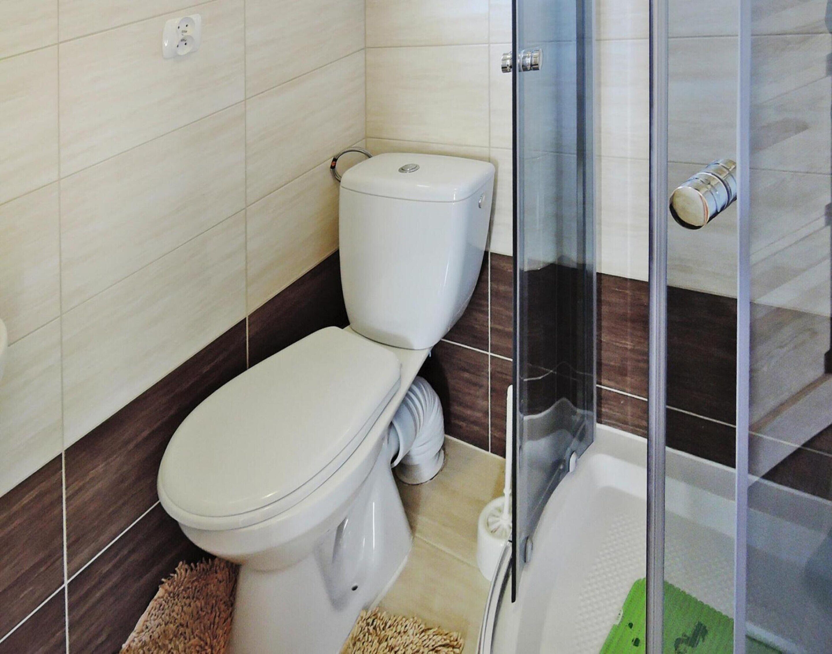 Et badeværelse med toilet, bruser og et bruseområde med glasvægge.