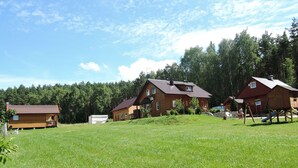 A rural cabin area with multiple wooden cabins, a grassy field, and a forest in the background. - Chalet by Baltic Sea Near Wiselka Lake (Międzyzdroje)