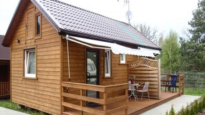 A wooden cabin with a covered porch, a satellite dish, and a small outdoor seating area. - Chalet by Baltic Sea Near Wiselka Lake (Międzyzdroje)