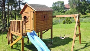 A wooden playhouse with a slide and a swing set in a grassy area. - Chalet by Baltic Sea Near Wiselka Lake (Międzyzdroje)