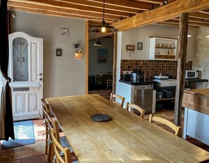 A dining area with a wooden table and chairs, a kitchen with modern appliances, and a rustic ceiling.