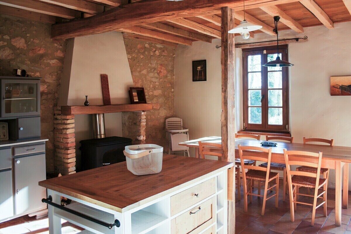 A rustic kitchen with a wooden table, chairs, and a stone wall.
