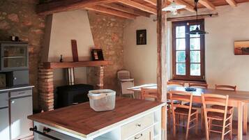 A rustic kitchen with a wooden table, chairs, and a stone wall.