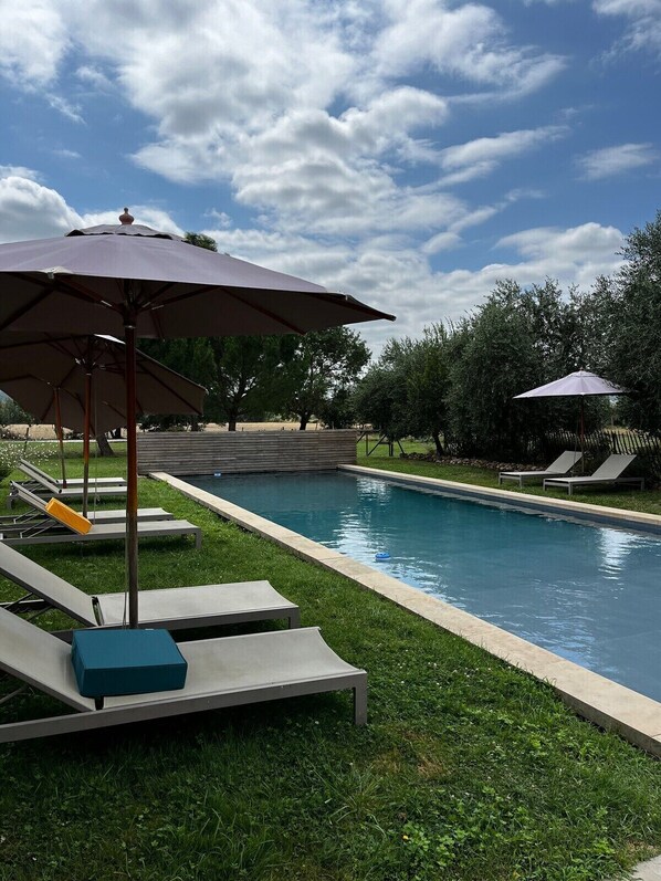 A swimming pool with lounge chairs and umbrellas, surrounded by grass and trees.