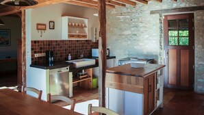 A rustic kitchen with wooden beams, a stone wall, and a wooden dining table with chairs. - 3-star country house, swimming pool (Fiac)