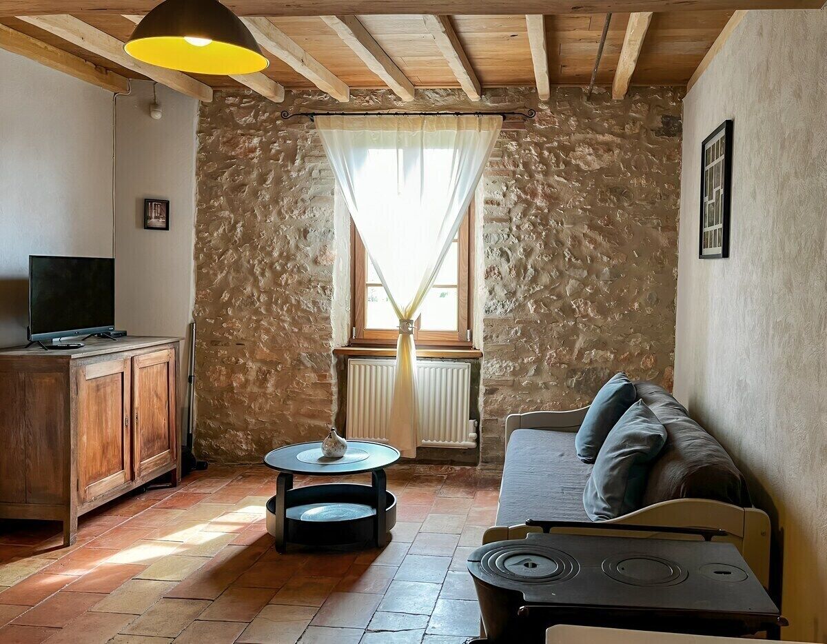 Ein gemütliches Wohnzimmer mit Steinwand, Holzbalken, einer Couch, einem Fernseher und einem Tisch mit Lampe.