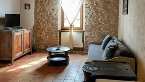 A cozy living room with a stone wall, wooden beams, a sofa, a TV, and a table with a lamp. - 3-star country house, swimming pool (Fiac)