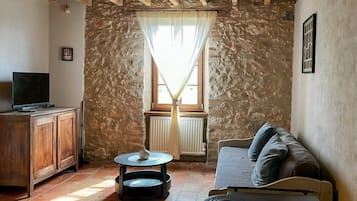 Ein gemütliches Wohnzimmer mit Steinwand, Holzbalken, einer Couch, einem Fernseher und einem Tisch mit Lampe.
