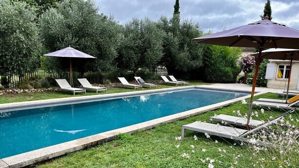 A rectangular swimming pool with a stone edge, surrounded by a grassy area with three lounge chairs and two umbrellas. - 3-star country house, swimming pool (Fiac)
