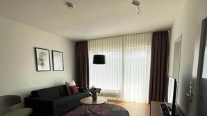 A modern living room with a dark sofa, a round coffee table, and a flat-screen TV on a wooden stand. - Komfortable Wohnung mit SPA und Pool (Langeoog)