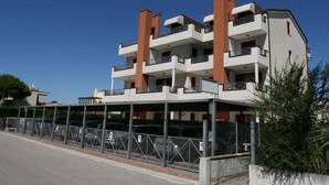 Edifício residencial com várias andares, varandas, área de estacionamento coberta e entrada com portão.