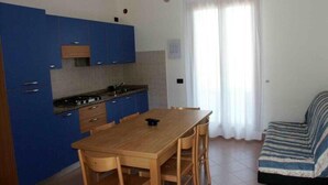 Cozinha compacta com armários azuis, mesa de jantar de madeira e um sofá.
