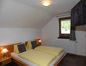Ein Schlafzimmer mit zwei Betten, einem fenster mit Vorhängen, einem Heizkörper und einem an der Wand befestigten Fernseher.