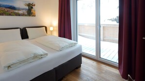 A hotel room with a bed, a painting on the wall, a window with curtains, and a view of the outside. - Kitzbuhel Alpine Lodge With Private Infrared Sauna (Mittersill)