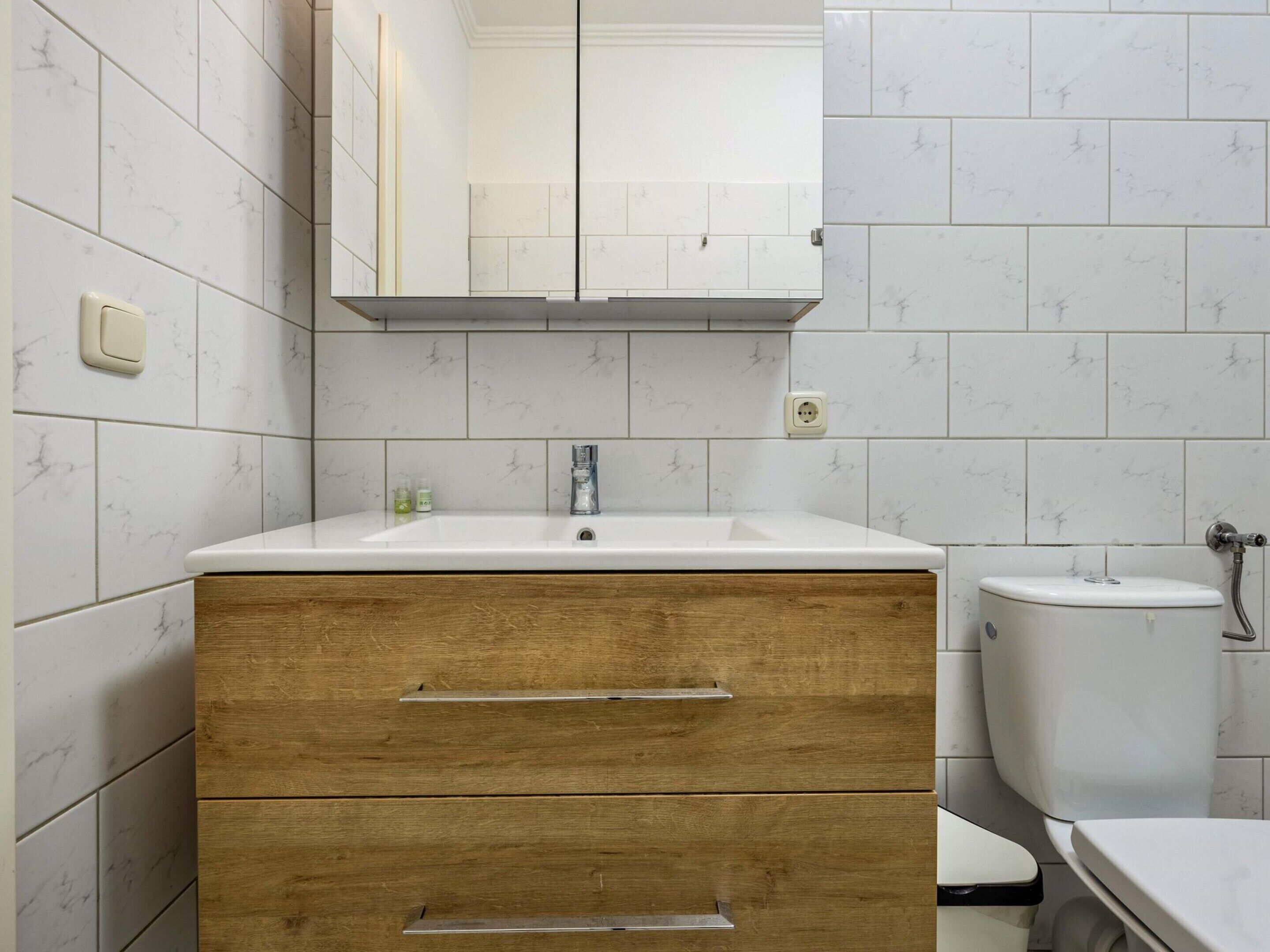 Une salle de bain avec un mur recouvert de carreaux de marbre blanc, un meuble-lavabo en bois et des toilettes.