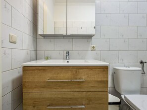 A bathroom with a white marble tiled wall, a wooden vanity with a sink, and a toilet. - Ferienwohnung in der Mecklenburger Seenplatte (Buchholz)