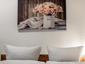 A bedroom with a bed, pillows, a wall-mounted picture of pink roses, and a wooden wall. - Ferienwohnung in der Mecklenburger Seenplatte (Buchholz)