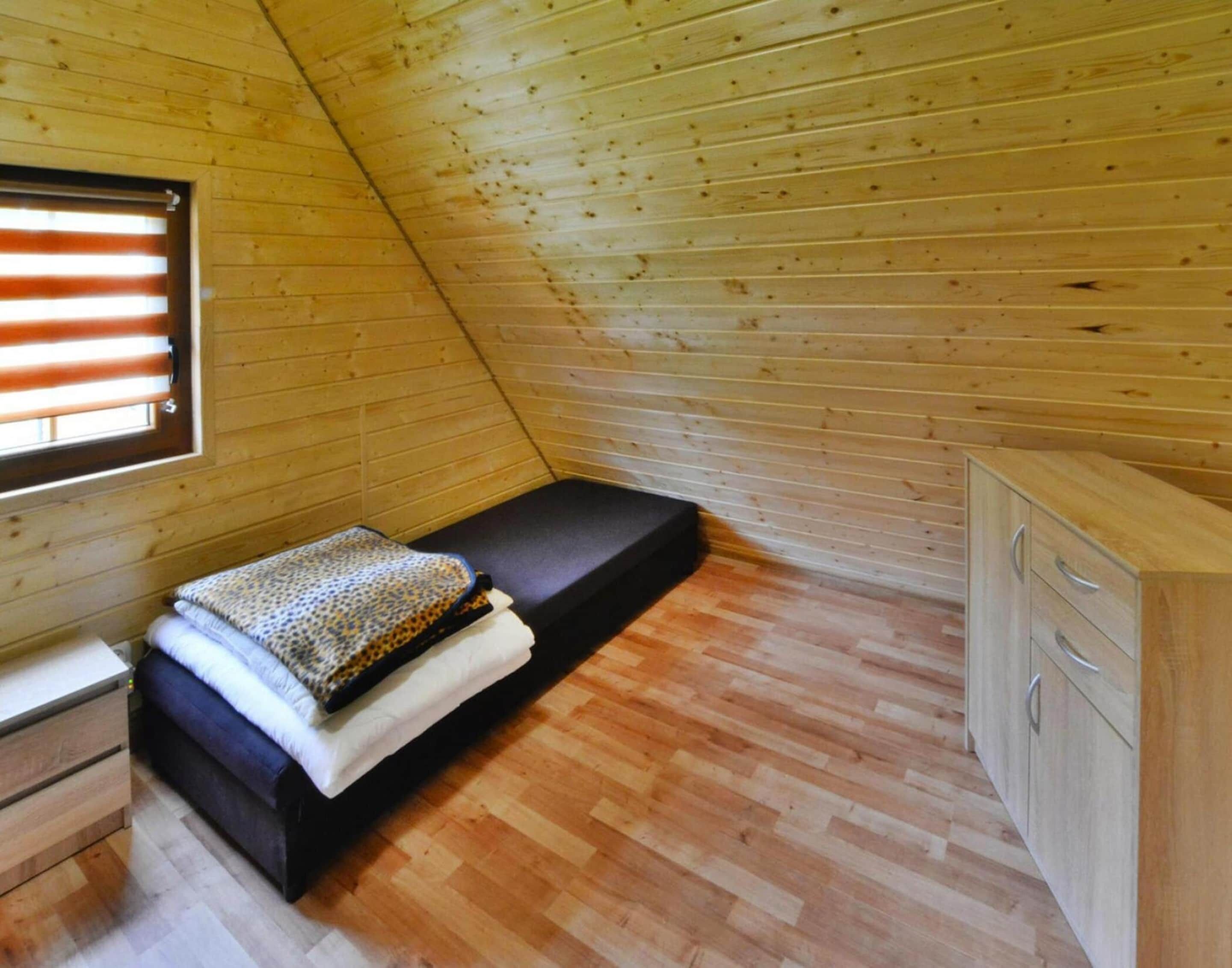 Ein kleiner Raum mit schrägem Dach, einem Bett, einem Nachttisch und einem Holzschrank.