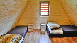 Une petite pièce mansardée triangulaire, avec des murs en bois et un plafond en pente. On y trouve deux lits avec des oreillers et une petite table au centre.