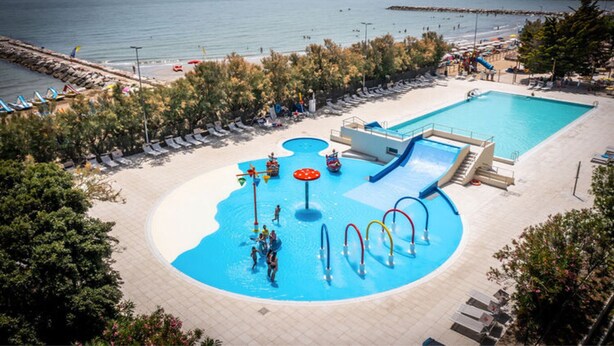 A pool area with a water slide, lounge chairs, and a view of the sea. - Bungalow in Caorle With Garden Furniture (Caorle)