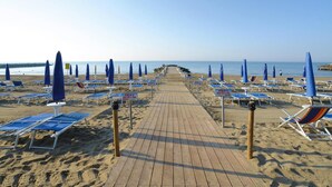 A beach with a wooden walkway lined with blue umbrellas and sun loungers. - Bungalow in Caorle With Garden Furniture (Caorle)
