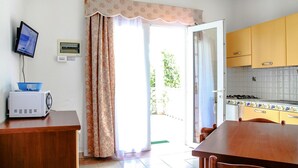 A kitchen with a dining table, a microwave, a TV, and a sliding glass door leading to a patio. - Bungalow in Caorle With Garden Furniture (Caorle)