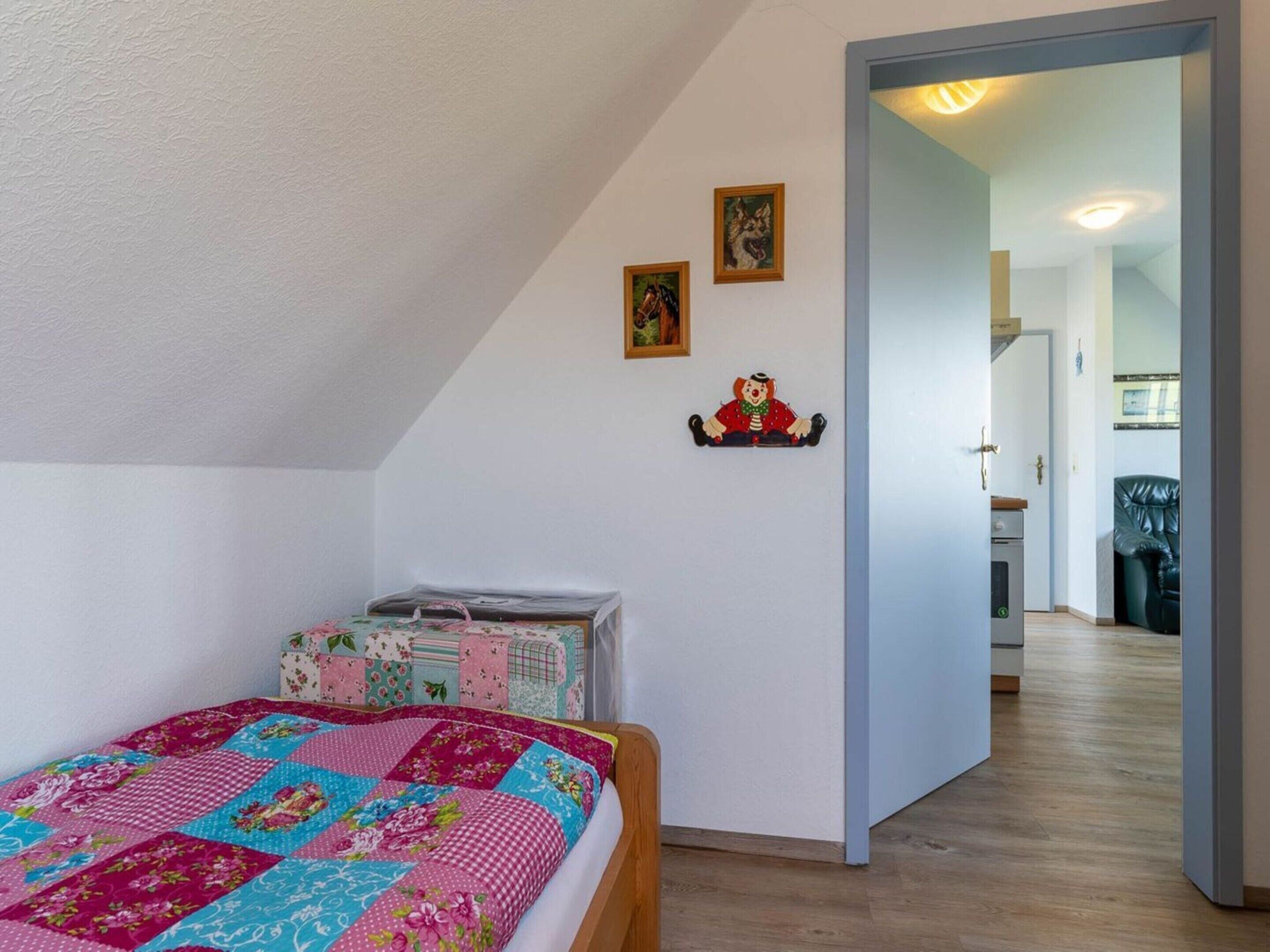 A bedroom with a bed, a quilt, a dresser, and a door leading to a hallway.