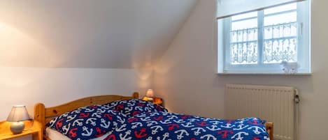 Un dormitorio con techo inclinado, una cama de madera, una mesita de noche con lámpara y una ventana con cortina decorativa.