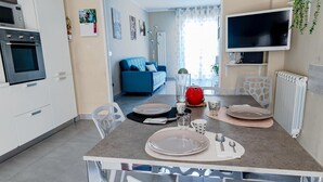 Una cocina moderna con armarios blancos, horno empotrado y comedor con una mesa dispuesta para dos.